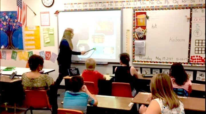 Caroline Musselwhite presents in front of a projector with a pointer, to students in a classroom.