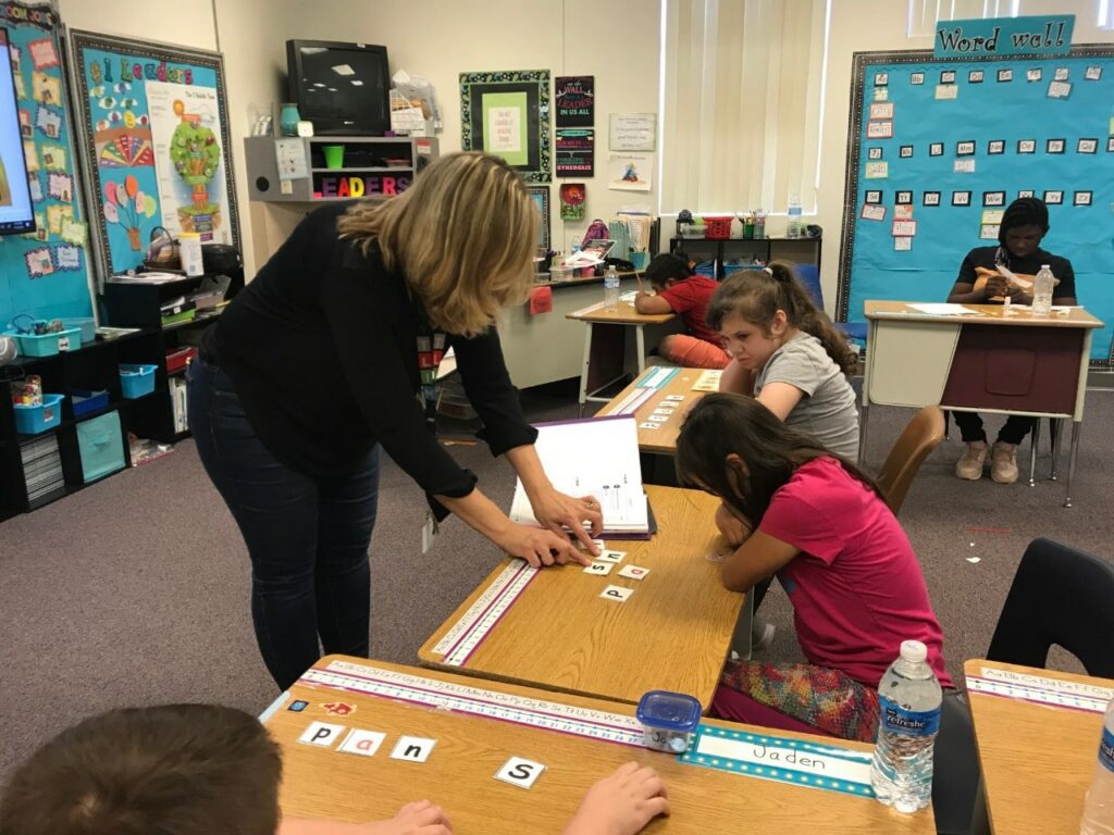 IMG_5929-1-1 - Building Wings A teacher helps students with reading lesson in a classroom.