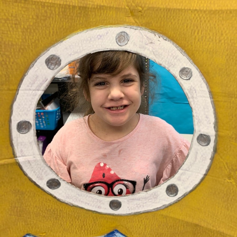 student-2-in-submarine-porthole-1 - Building Wings A student in a pink shirt smiles at the camera with an animated border around the image.