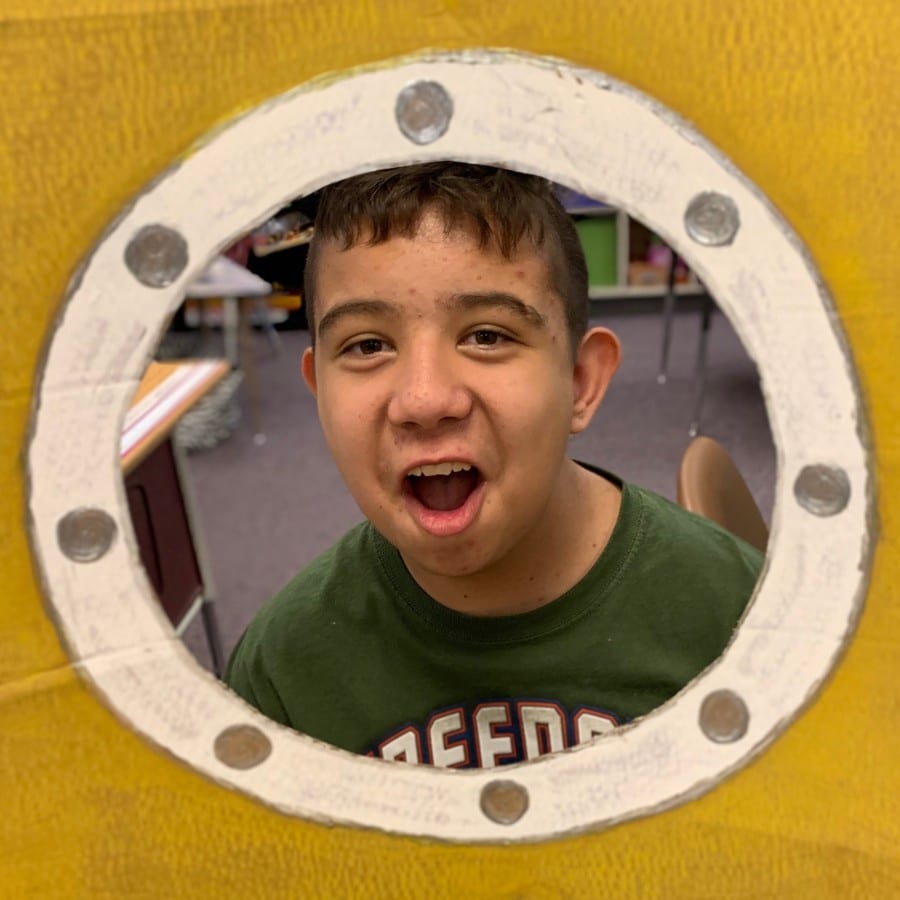 submarine-student-in-porthole-1 - Building Wings A student in a green shirt smiles at the camera with an animated border around the image.