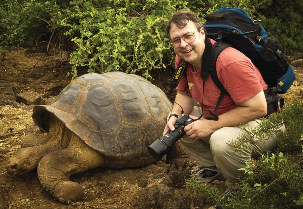 Don-witha-large-tortos - Building Wings Don Johnston poses next to a large turtle outdoors.