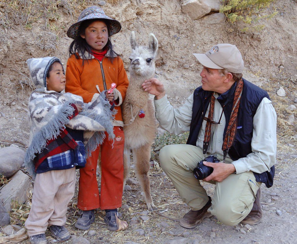 Bringing the curriculum together with stories from around the globe - Building Wings Jerry Stemach pets a small llama outdoors with two children dressed in hiking gear.