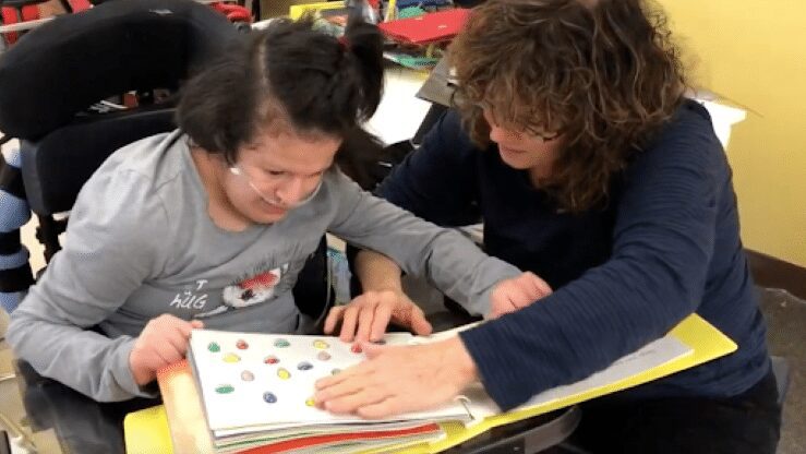A teacher works with a student with complex learning needs in a classroom.