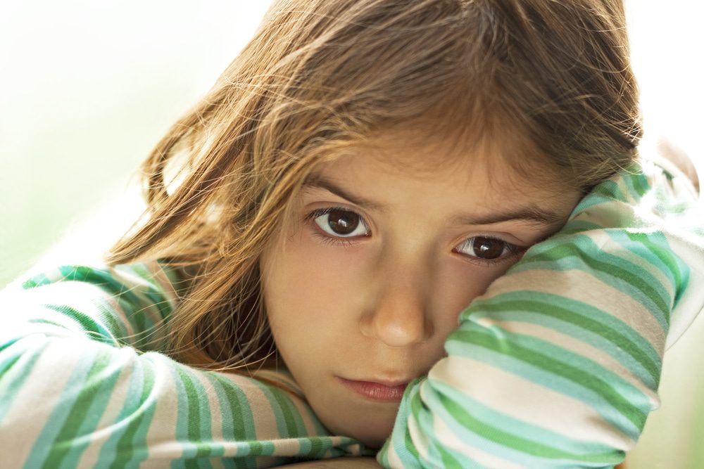 Depositphotos_22214777_S - Building Wings A young child in green striped shirt, stares at the camera, with her head in her hands.