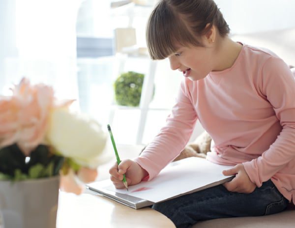 Writing - Building Wings A young girl wearing a pink shirt, writes on a piece of paper.