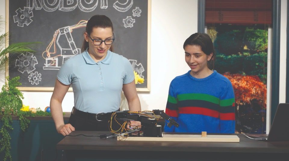 Video-Robots-05 1-min - Building Wings 2 students look animatedly at a incomplete robot in front of them on a table.