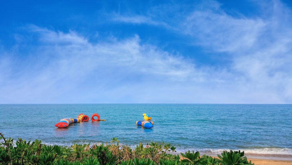 Tropical Trinity Beach on sunny day - Building Wings A beach scene with open water and a floating trampoline anchored off the shore in an image with blue skies and wispy clouds