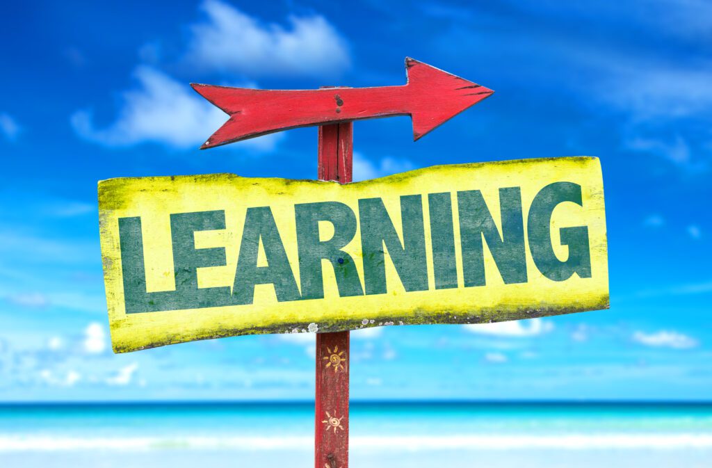 learning this way - Building Wings beach scene with a yellow sign with green text: Learning, with a red arrow pointing to the right.