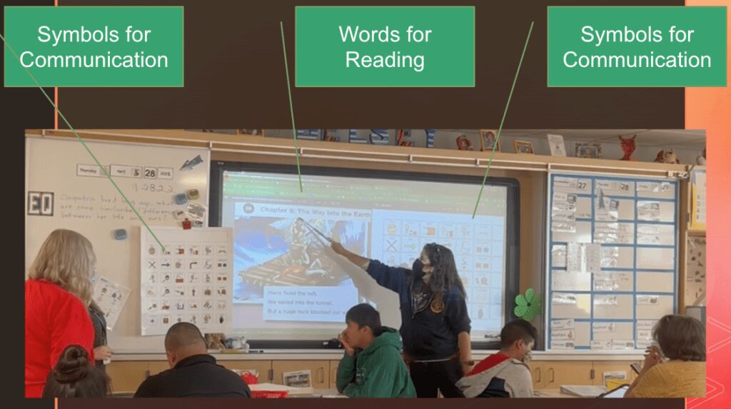 classroom with communication symbols and words for reading - comprehensive literacy instruction - Building Wings classroom setting with teacher pointing to words for reading projected on a screen with supportive words for communicating displayed on both sides of the screen.