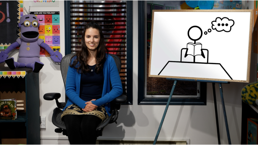 ReadtopiaGO Teaching Tutorial - Building Wings A classroom setting with a teacher facing the class with Geartrude the puppet on a bookshelf behind her.