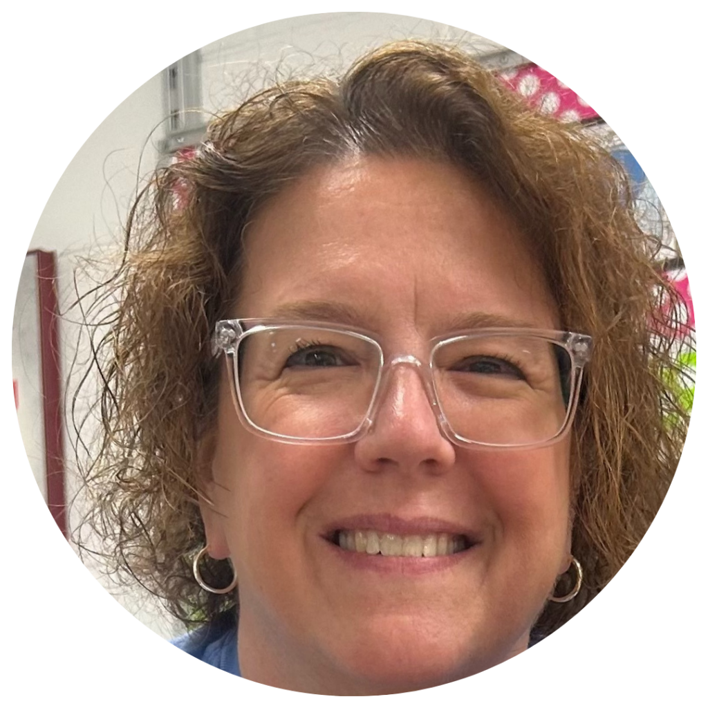 Woman with curly hair and clear framed glasses smiles in a classroom